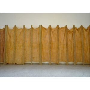 Photo of Eva Hesse’s sculpture, Expanded Expansion of 1969. The sculpture is made of fiberglass and latex expanded on cheesecloth. 3 units of 3, 5, and 7 poles each are assembled in line on the wall.