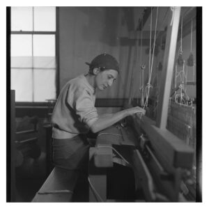 Black and white photo of Anni Albers weaving at loom, Black Mountain College in 1937. Photograph by Helen M.