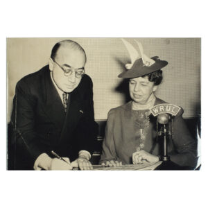 Black and white photo of Szyk (left) presenting to First Lady Eleanor Roosevelt (right) signed poster stamps created to raise funds for the British-American Ambulance Corps, 1941